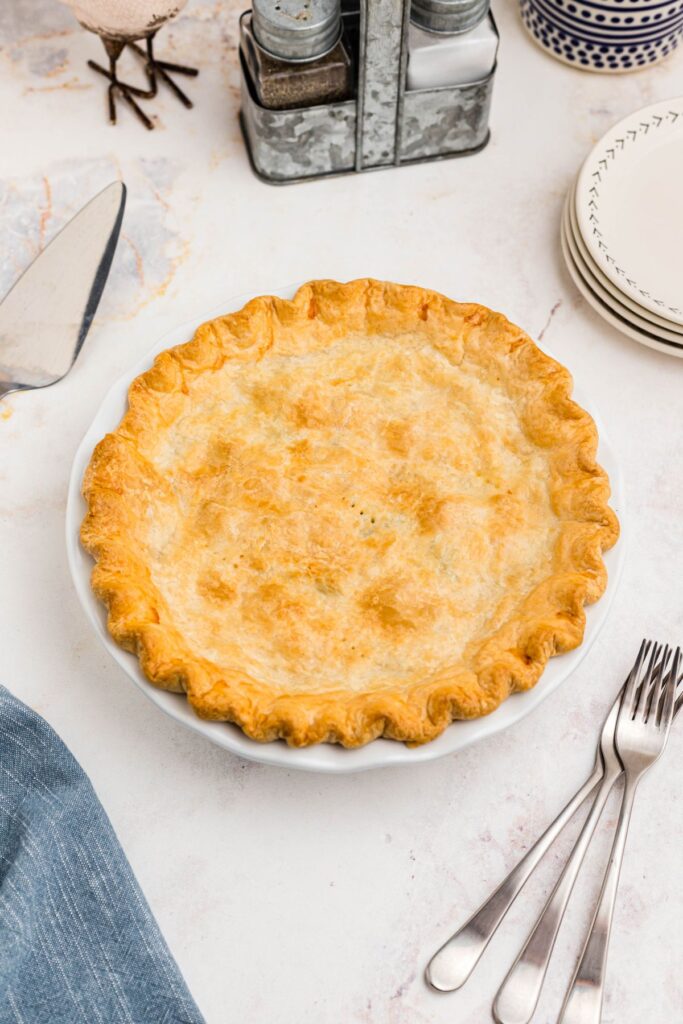 Golden baked chicken pot pie on a marble table with forks and small plates. 