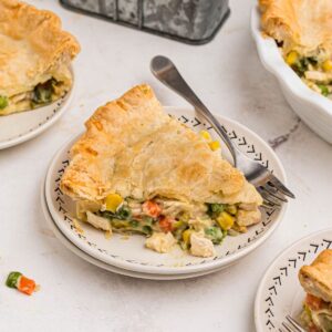 Golden crusted pot pie filled with chicken and veggies on a small white plate with a fork.