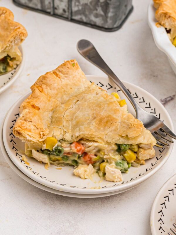 Golden crusted pot pie filled with chicken and veggies on a small white plate with a fork.