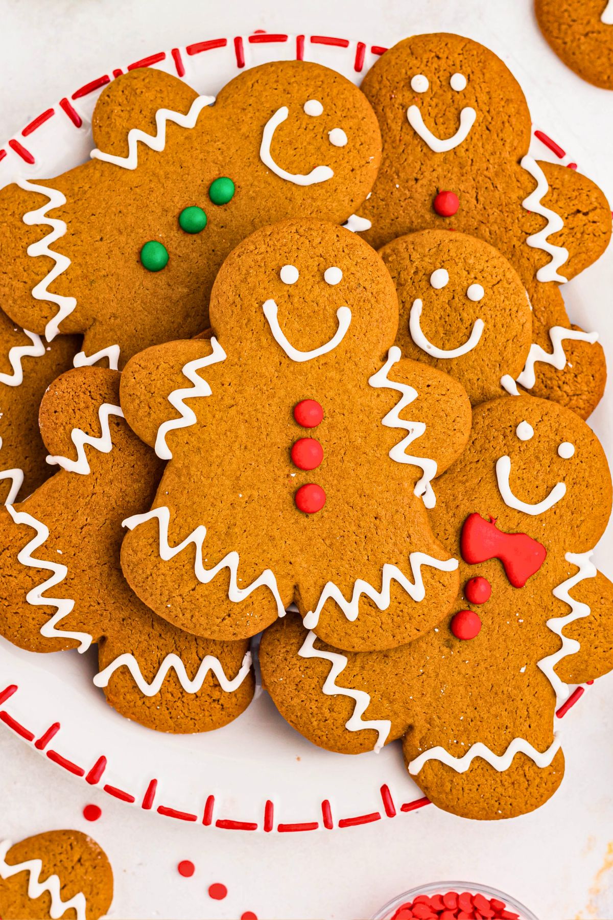 Gingerbread cookies stacked on a white plate with sprinkles and other cookies scattered around the plate. 