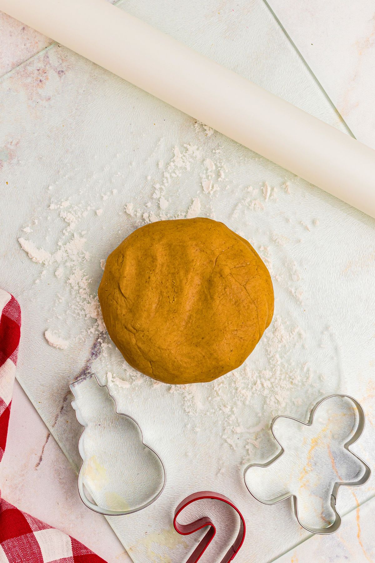 Golden round disc of gingerbread cookie dough, with cookie cutters and rolling pin on marble table. 