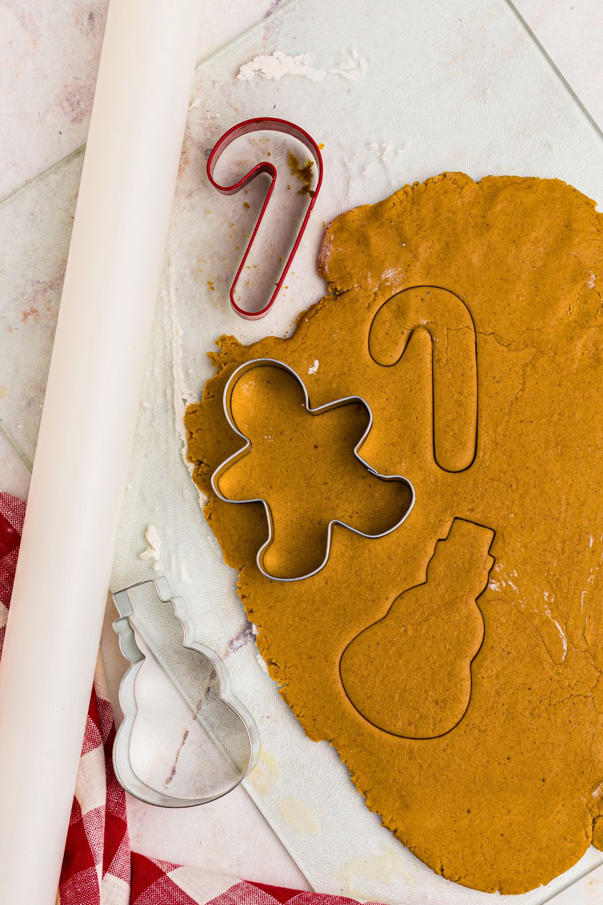 gingerbread cookie dough rolled out and being shaped with cookie cutters. 