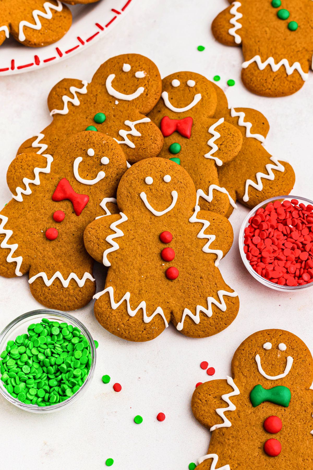 Golden brown gingerbread men cookies stacked on a marble table with holiday sprinkles scattered around the table. 