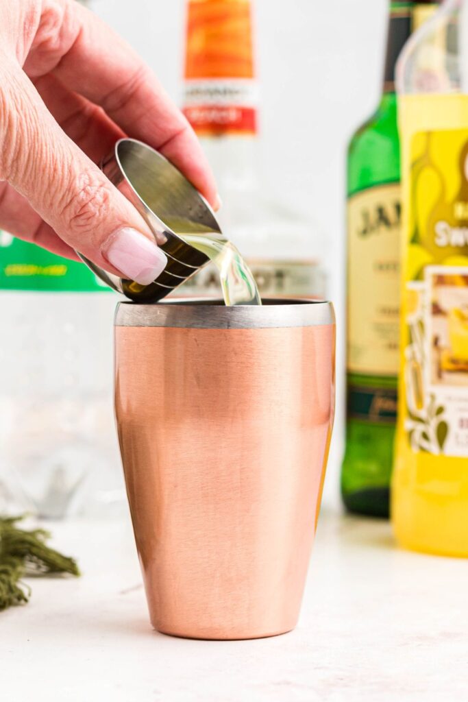 Ingredients being added to a cocktail shaker to make a green tea shot.