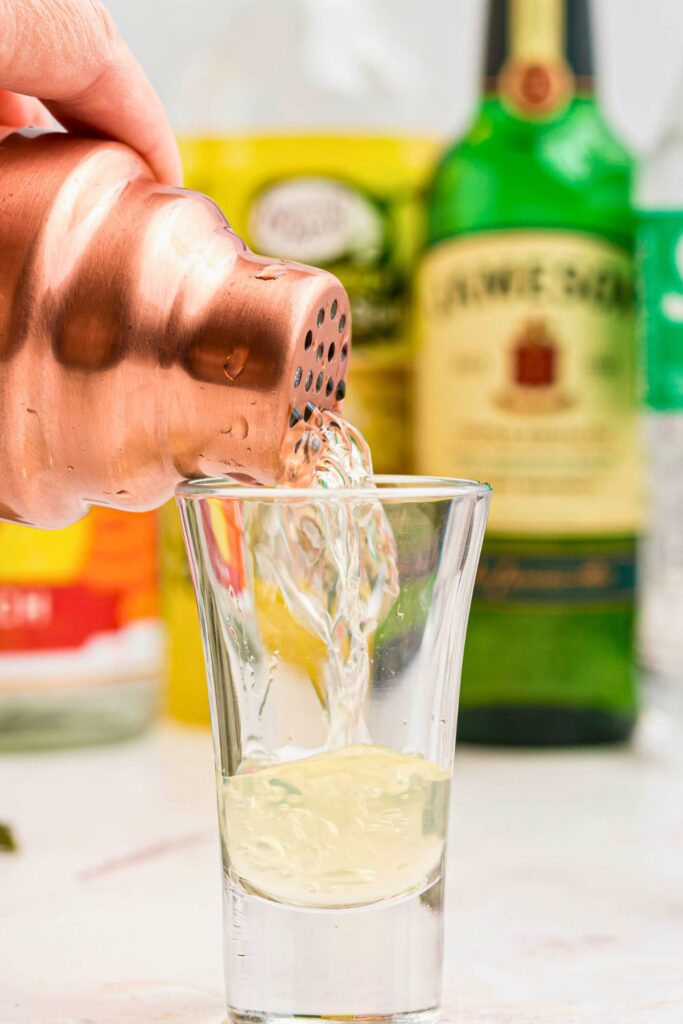 Mixed drink being strained from a cocktail shaker into a shot glass.