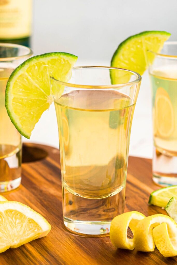 Green tea shot in a small shot glass with a lime wedge and lemon curls in front of the glass. 