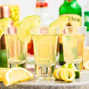 Green tea shots in small shot glasses garnished with lime wedges on a marble serving tray.