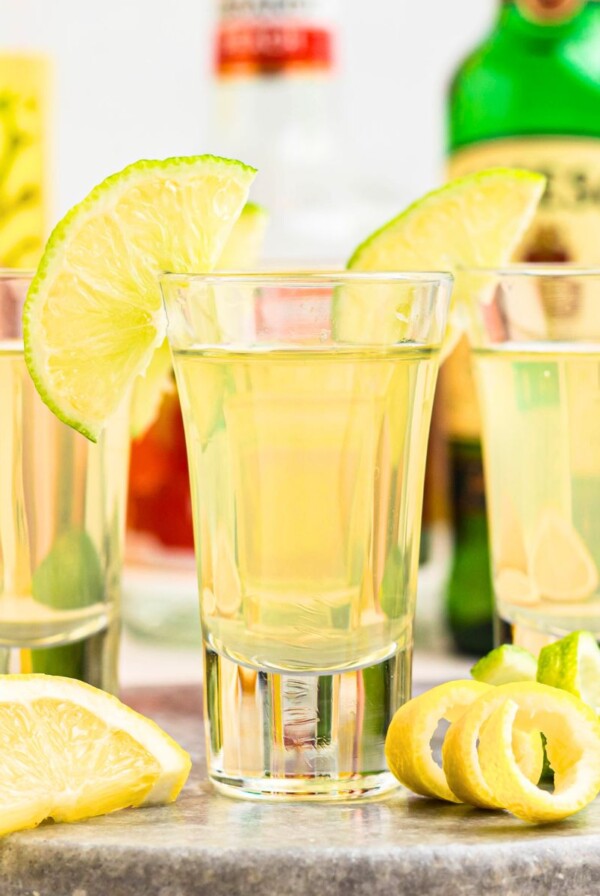 Green tea shots in small shot glasses garnished with lime wedges on a marble serving tray.