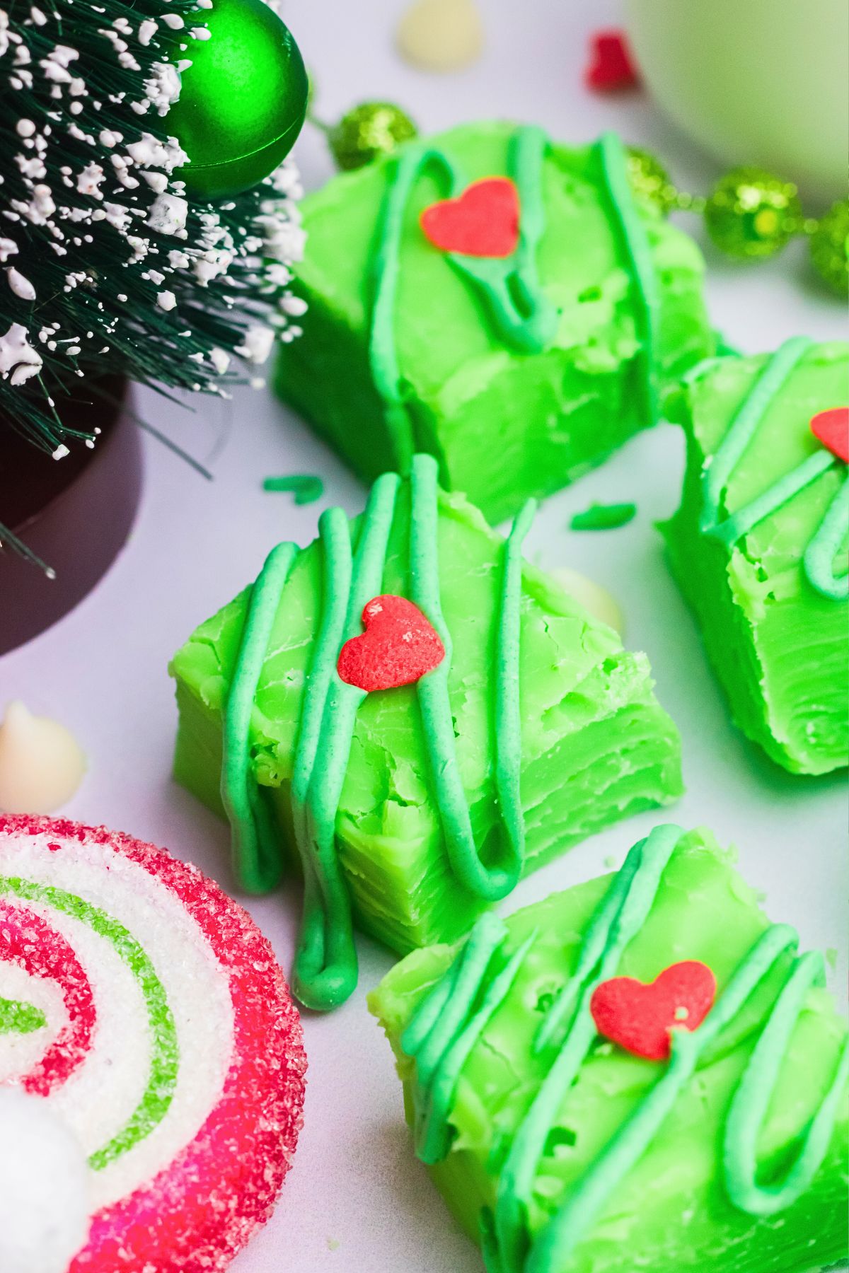 Bright green fudge with a small heart on top in front of a decorative tree.