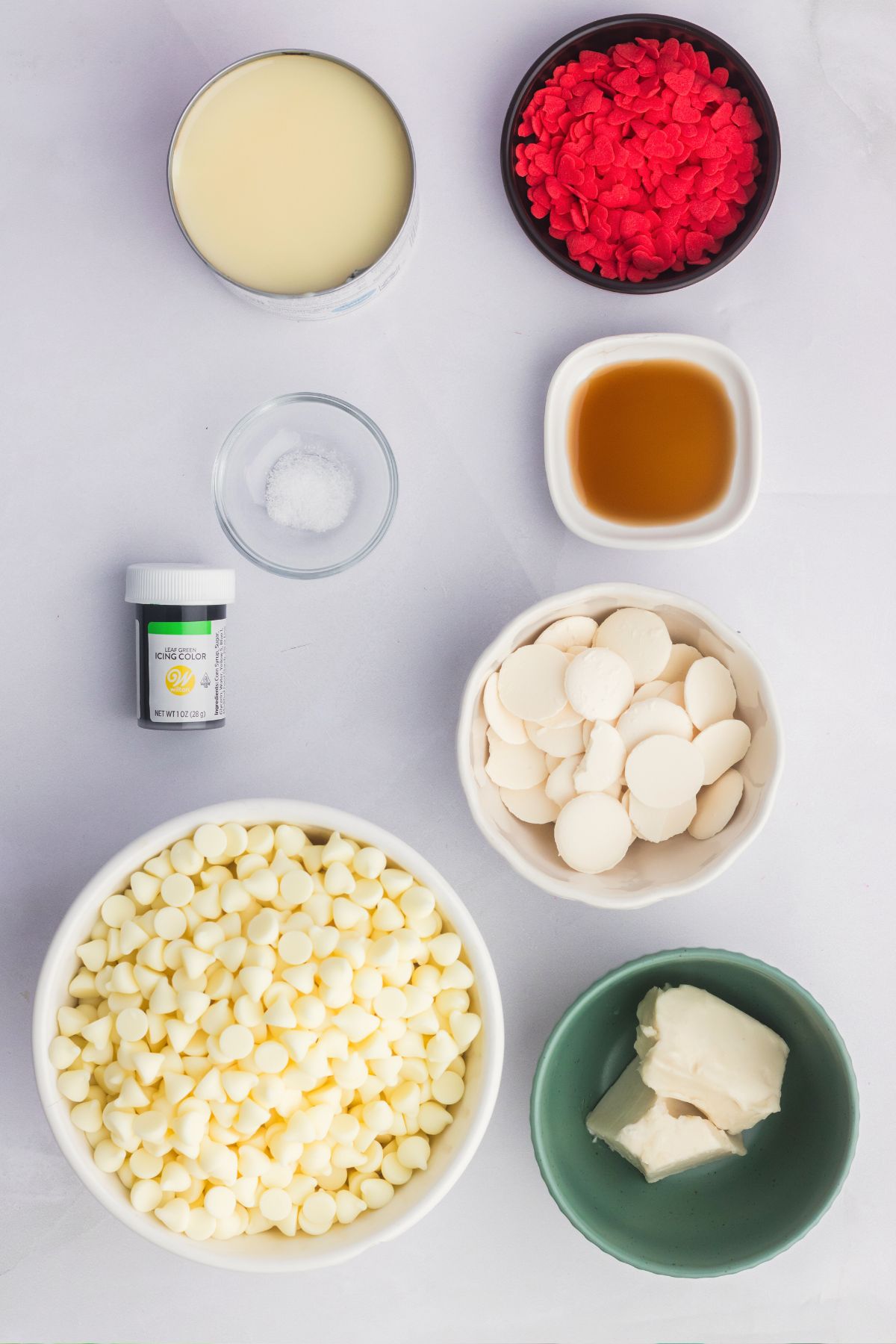 Ingredients needed to make Grinch fudge measured out in small bowls on a white table. 