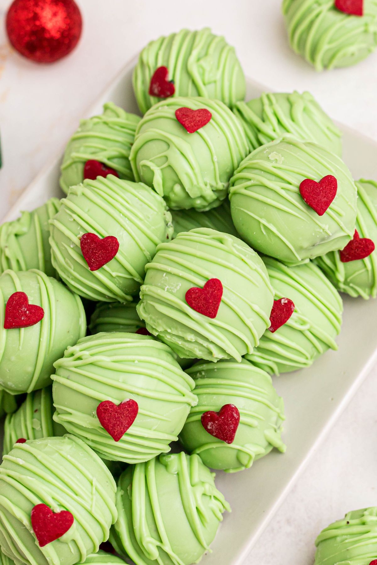 Green coated Grinch Oreo balls with a red candy heart, stacked on a plate.