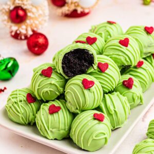 Green coated Grinch Oreo balls with a red candy heart, stacked on a plate.