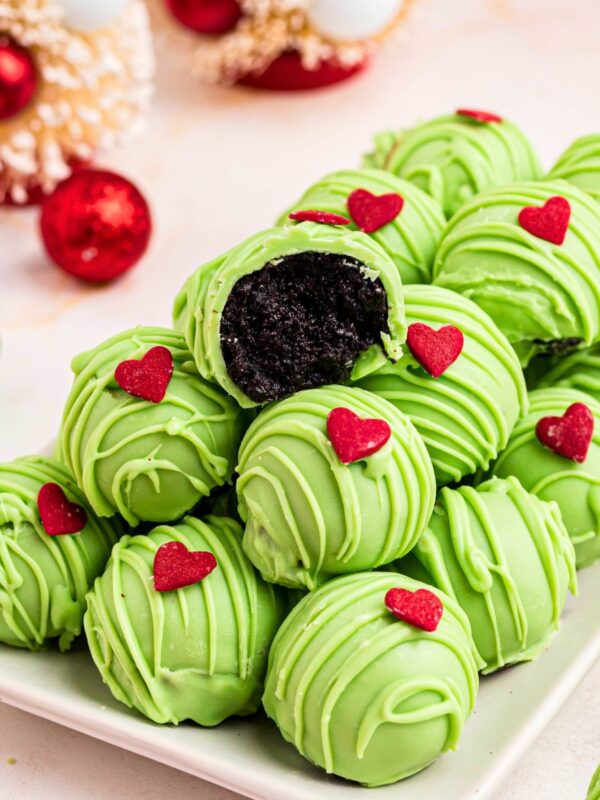 Green coated Grinch Oreo balls with a red candy heart, stacked on a plate.