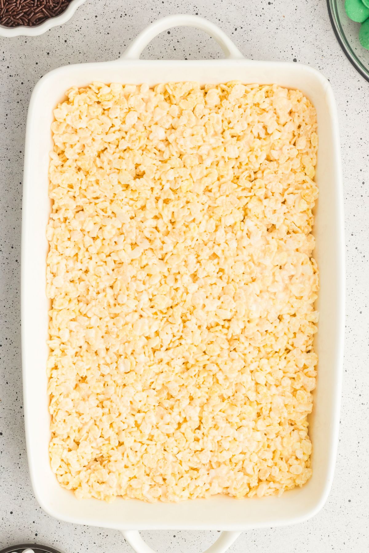 Rice krispie cereal mixed with melted marshmallows and butter in a white casserole dish. 