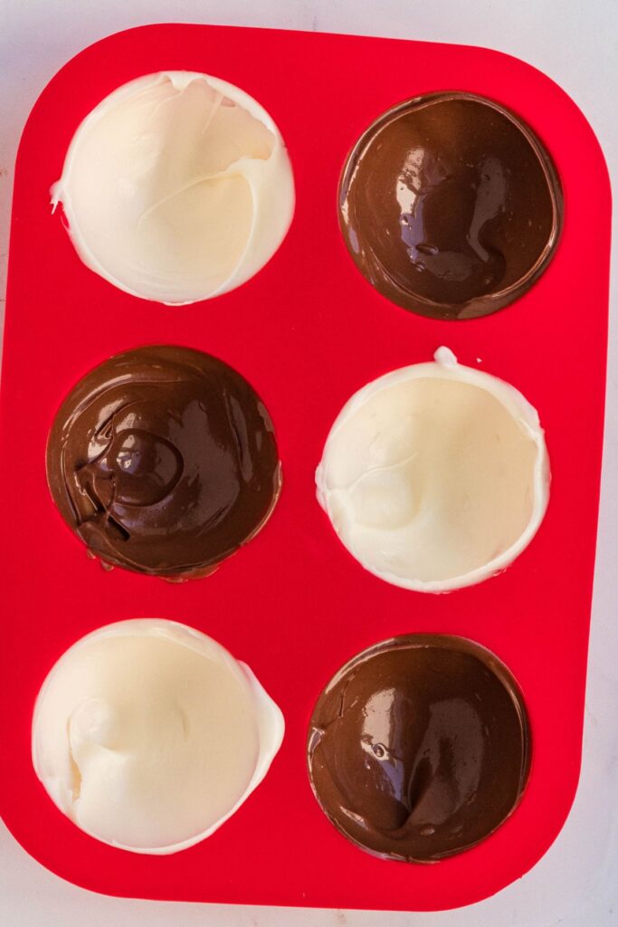 Melted chocolate in a red silicone mold to make cocoa bombs.