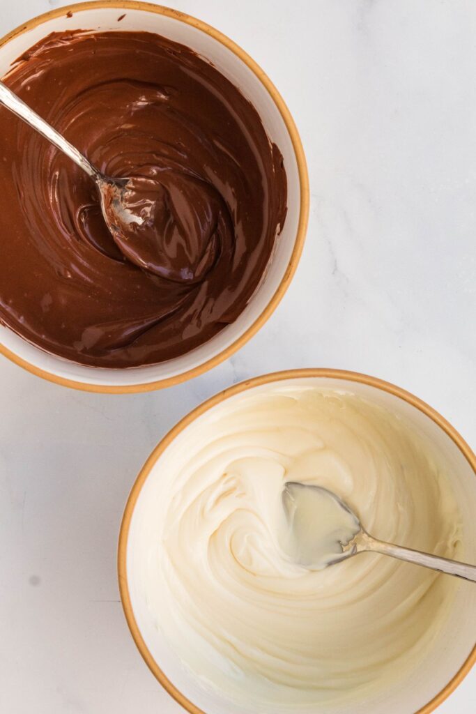 White and milk chocolate melted in bowls with spoons in them.