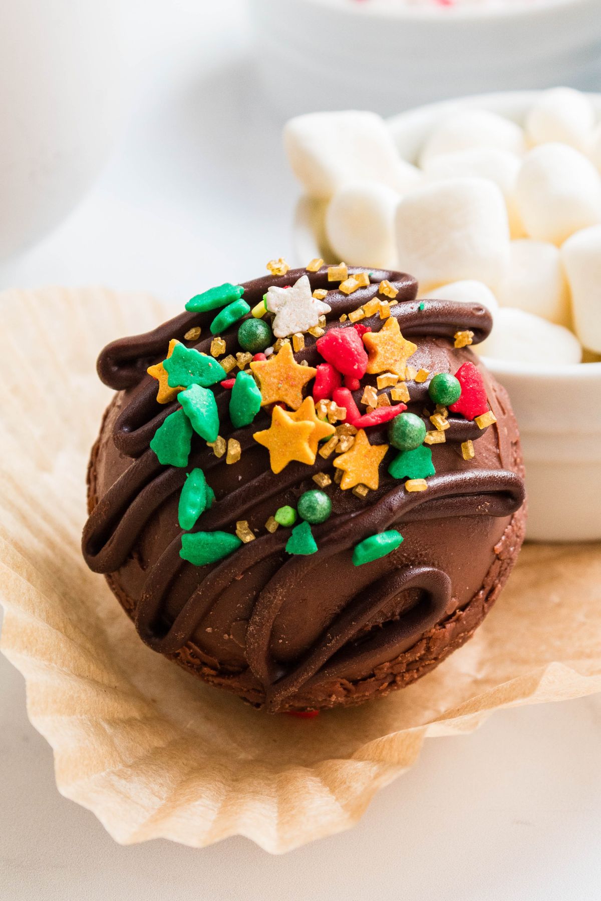 Chocolate cocoa bomb in front of mini marshmallows on the table.
