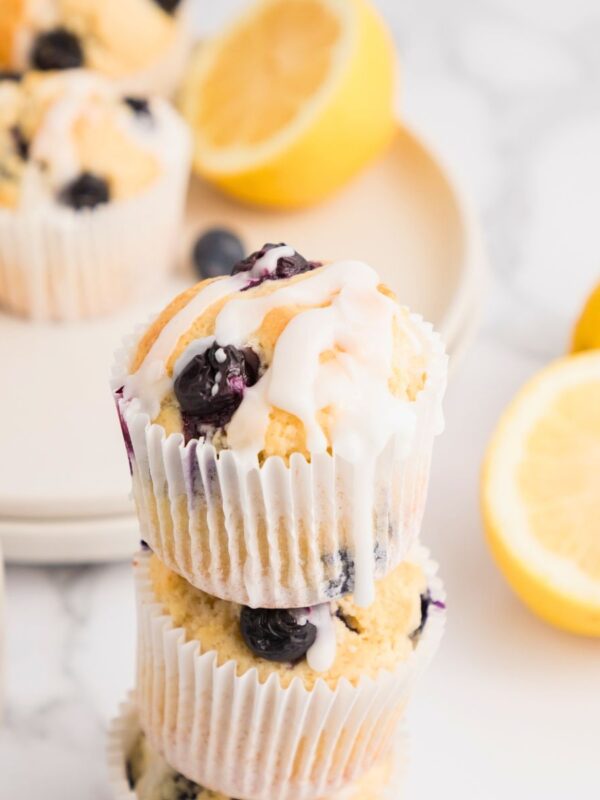 Golden lemon blueberry muffins baked and then stacked on the table with lemons stacked behind the muffins.