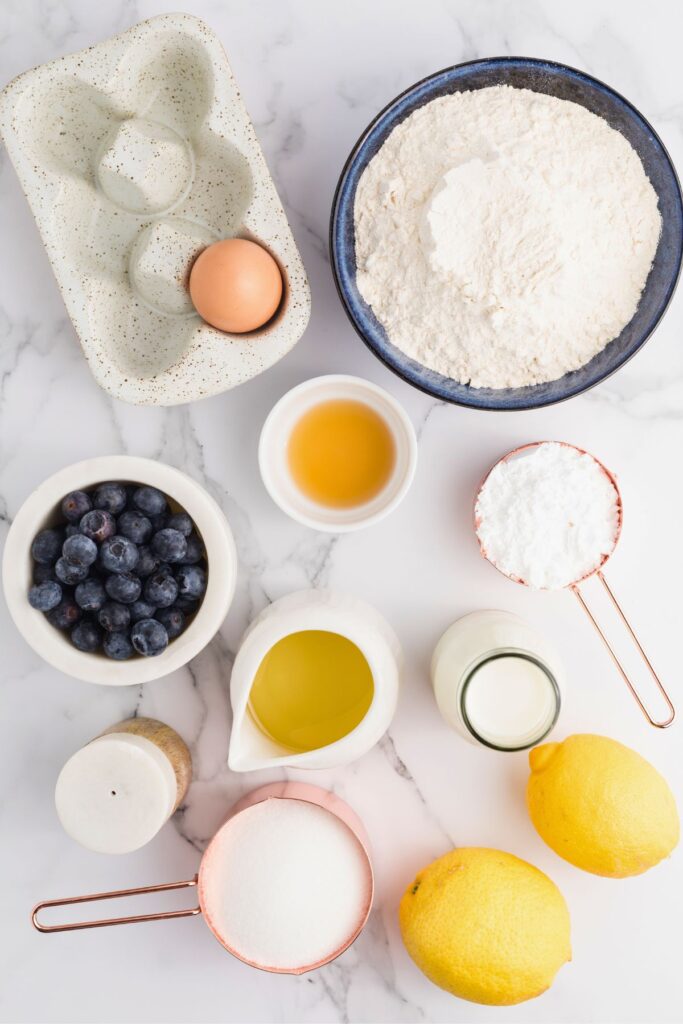 Ingredients needed to make lemon blueberry muffins measured on a white marble table.