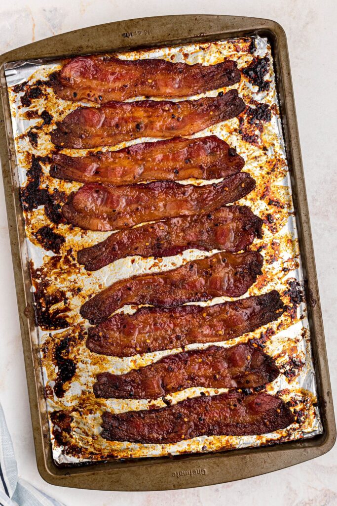 Golden juicy bacon slices on a baking sheet after cooking in the oven. 