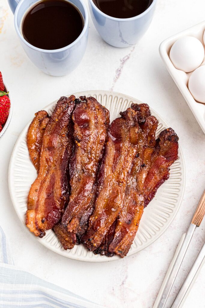 Golden brown slices of bacon on a white plate with tongs next to the plate. 