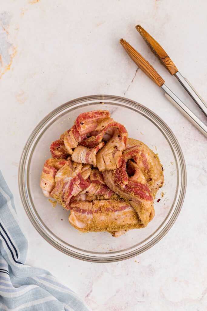 Bacon tossed with brown sugar and spices in a large glass bowl.