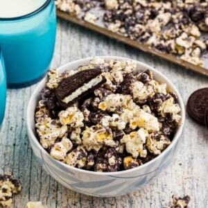 Popcorn combined with melted white chocolate and Oreo cookies crushed, with glasses of milk on the table.