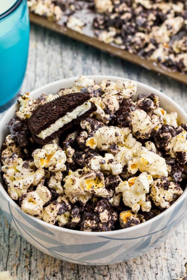 Popcorn combined with melted white chocolate and Oreo cookies crushed, with glasses of milk on the table.