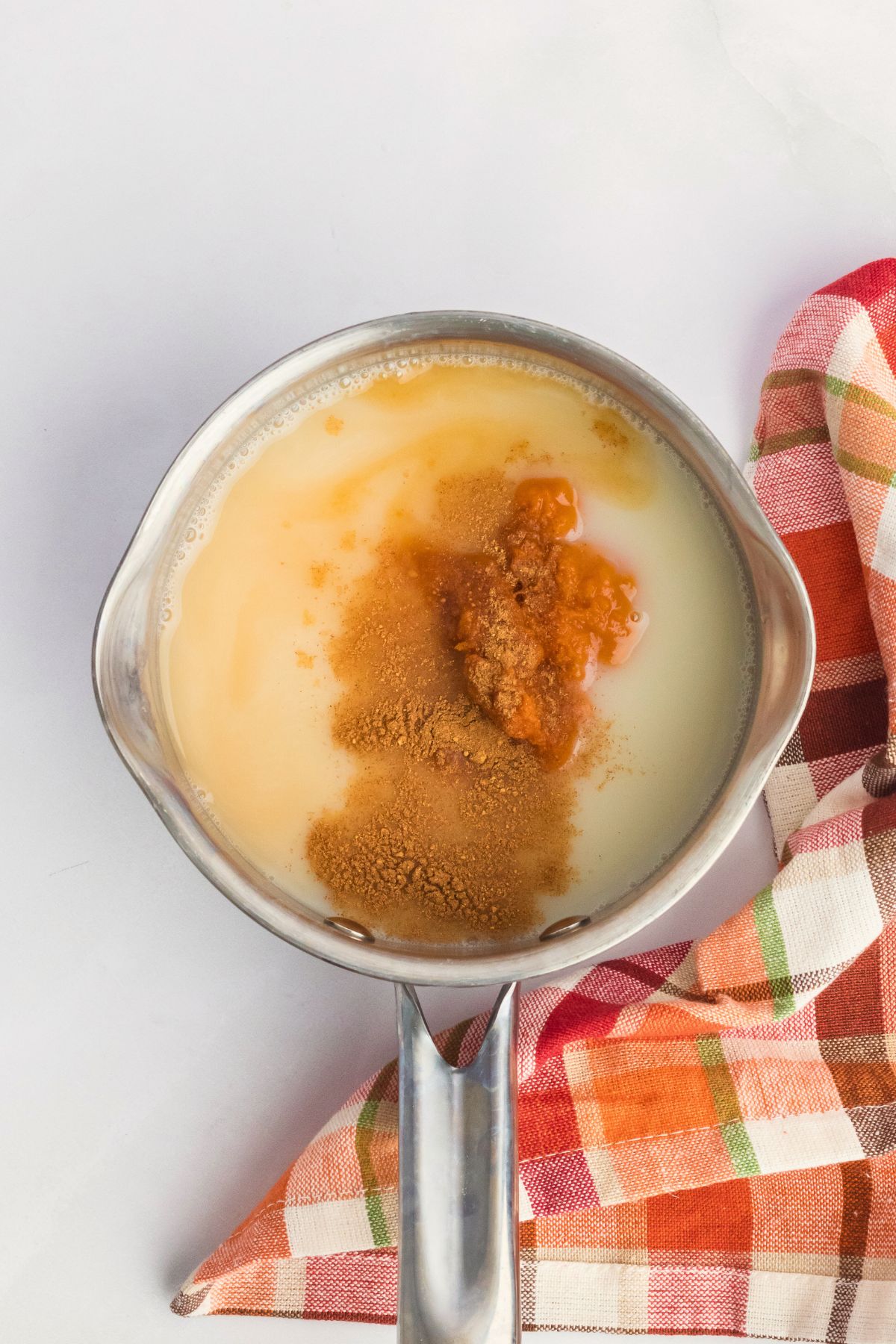 Pumpkin puree and other ingredients in a small saucepan on a white table. 