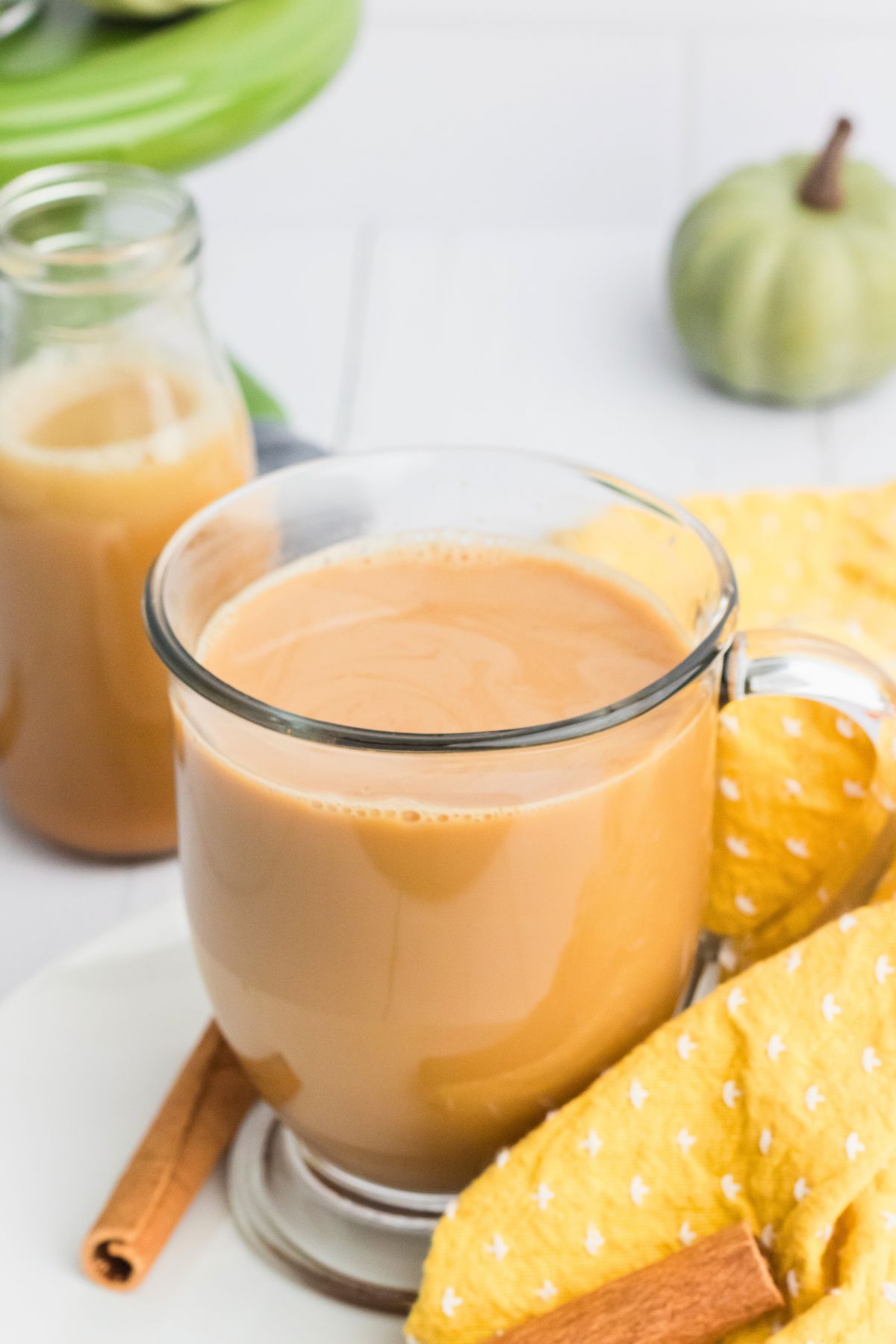 Creamy coffee in a clear glass cup with a bottle of creamer on the table behind it. 