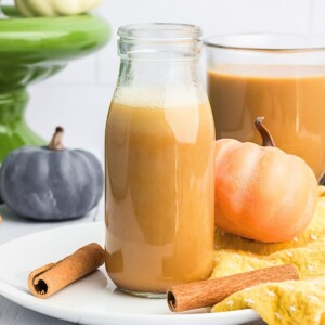 Creamy pumpkin spice creamer in a clear glass bottle with small pumpkins around it.