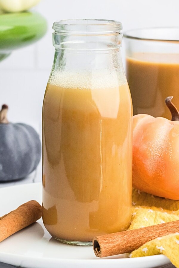 Creamy pumpkin spice creamer in a clear glass bottle with small pumpkins around it.