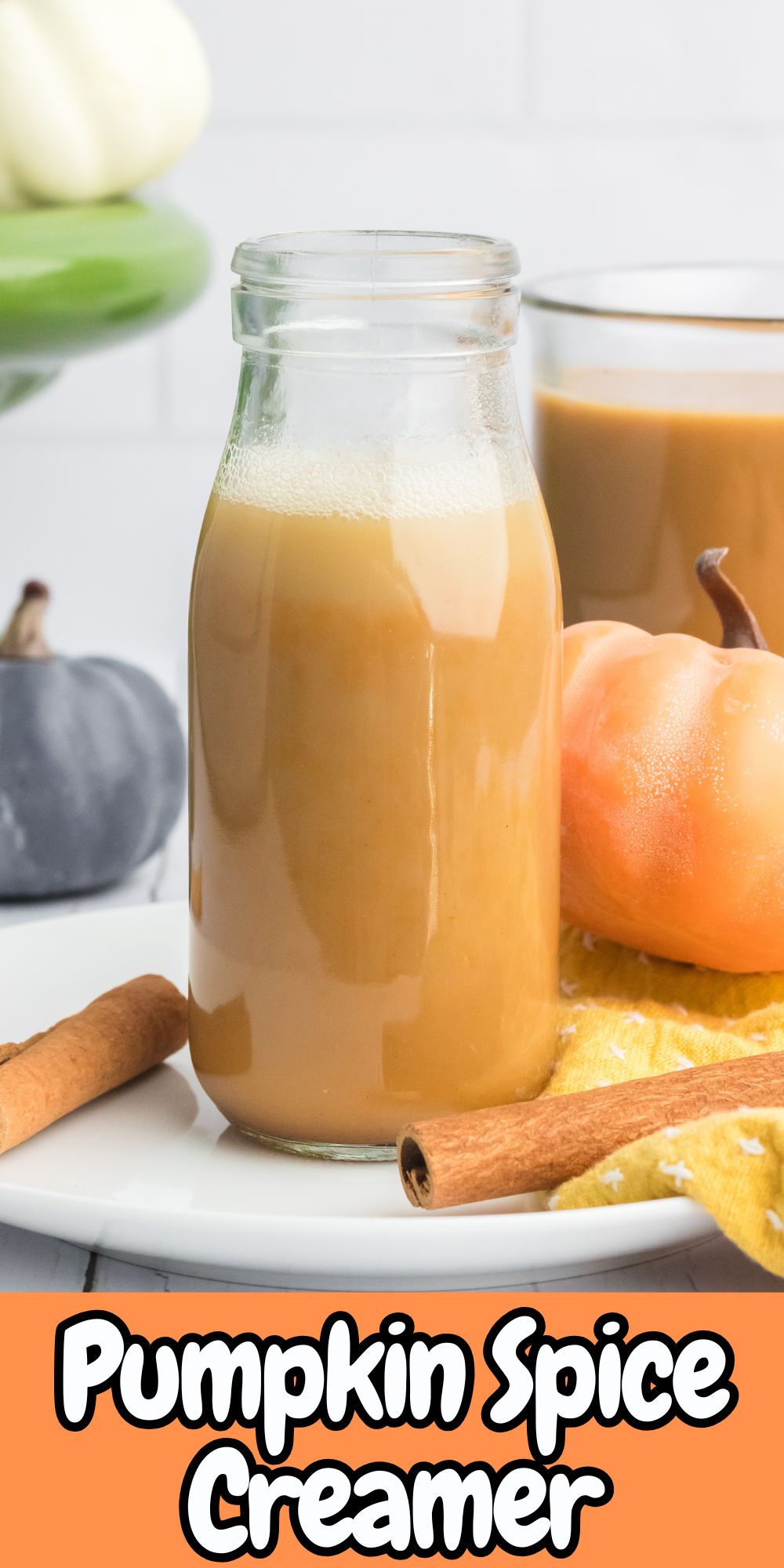 Pumpkin spice creamer in a glass bottle with cinnamon sticks and small pumpkins around it.