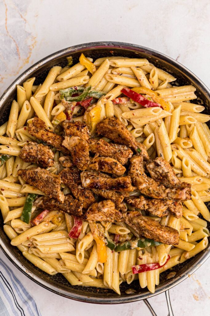 Chicken added to pasta and vegetables in a large skillet. 