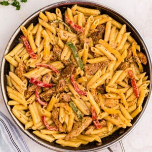 Cooked pasta topped with cheesy cream sauce and sautéed veggies and seasoned chicken in a large skillet.