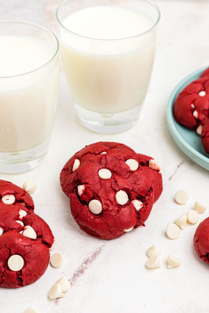 Bright red velvet cookies with white chips on a marble table with glasses of milk. 