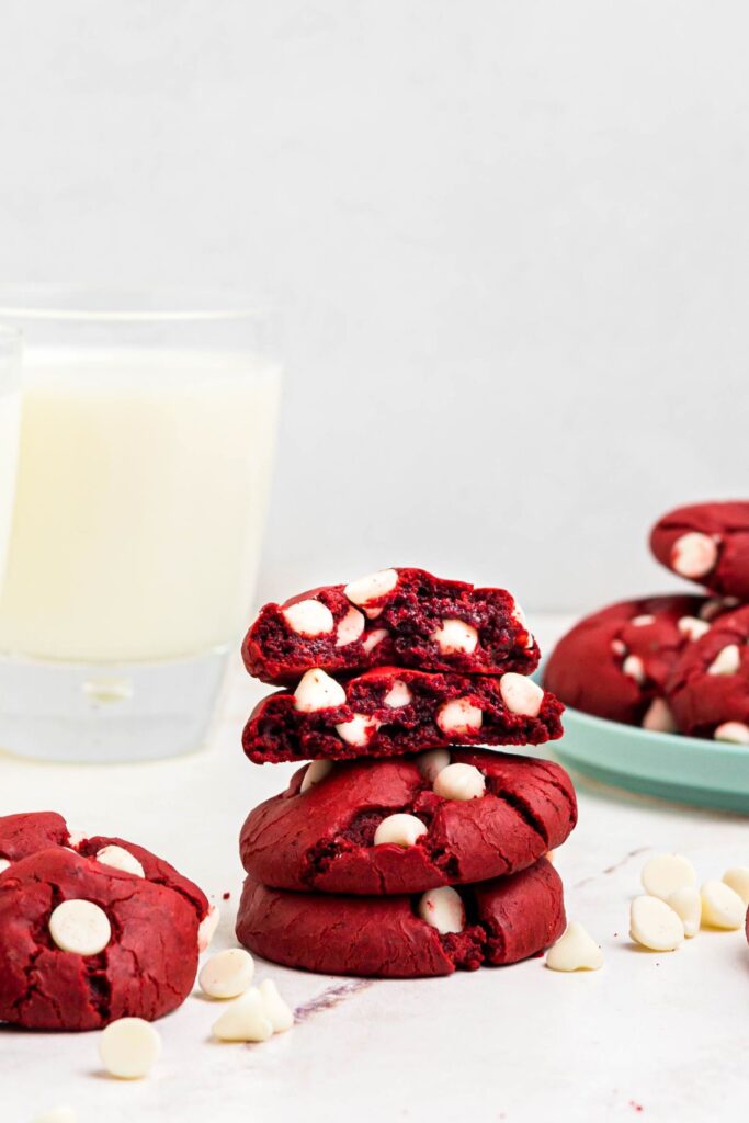 Red cookies stacked on a marble table with the top cookie cut in half showing moist inside and white chips. 