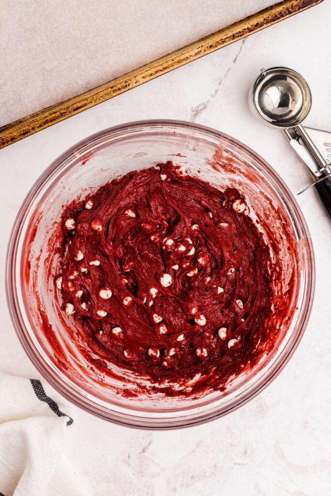 Cookie dough mix in a large glass bowl with a scoop next to the bowl. 