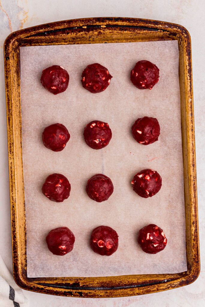 Red velvet cake mix balls of dough on a baking sheet before being cooked. 