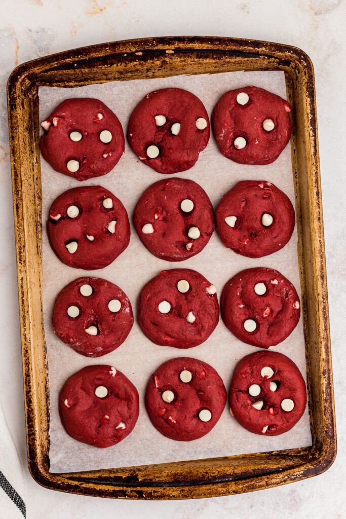 Red velvet and white chocolate chip cookies on a baking sheet after being cooked. 