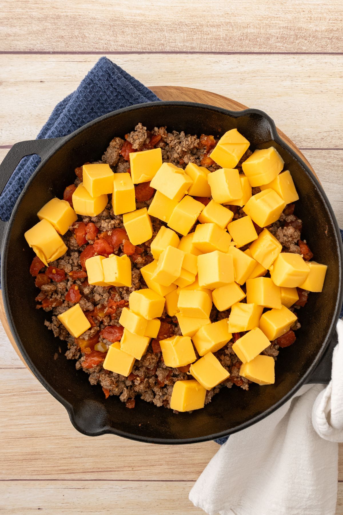 Cubes of cheese being added to a skillet with cooked ground beef. 