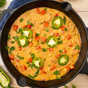 Cheesy Dip in a black skillet, topped with chopped tomatoes and diced jalapenos.