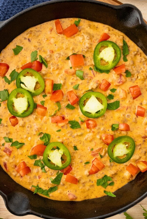 Cheesy Dip in a black skillet, topped with chopped tomatoes and diced jalapenos.