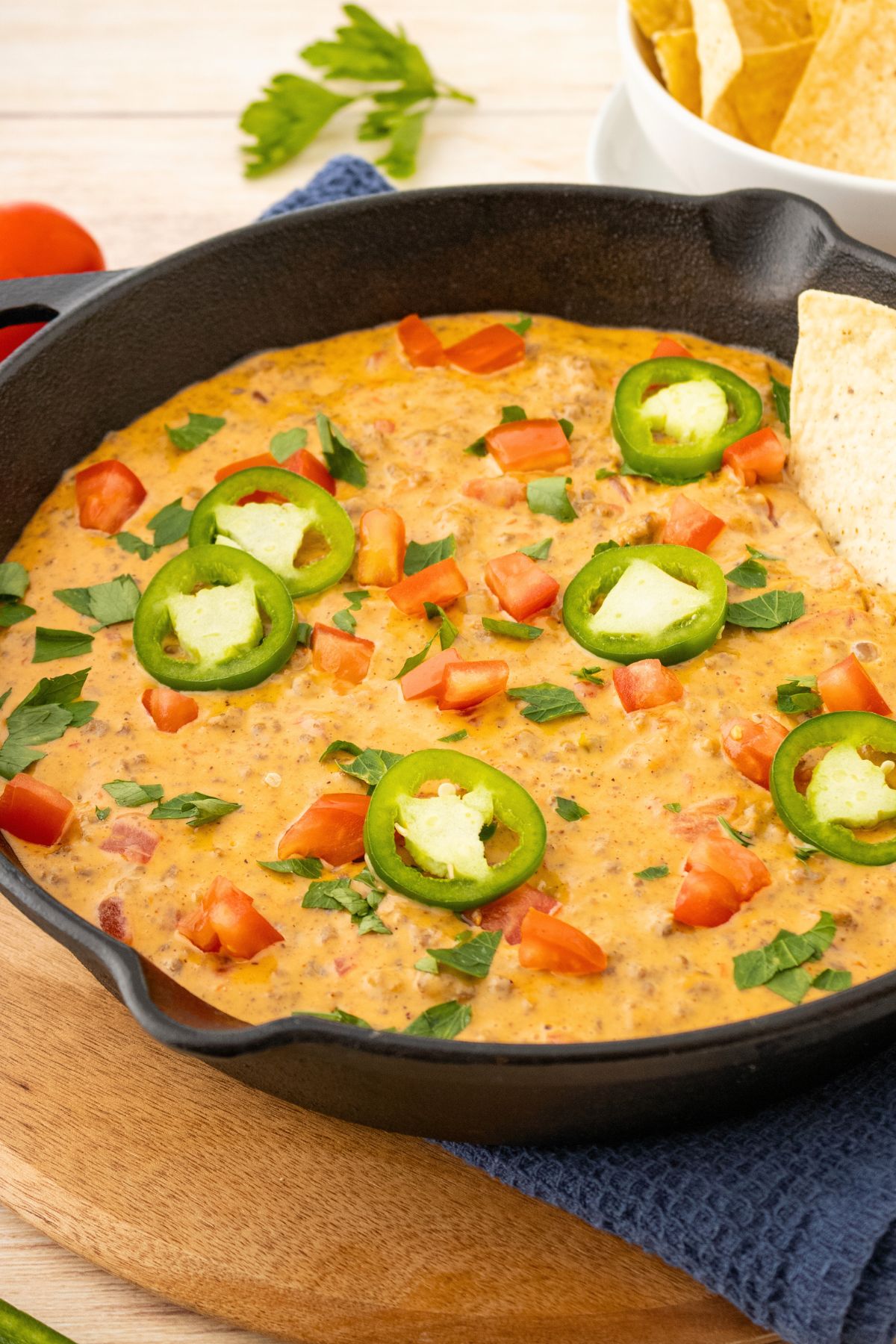 Black skillet filled with Rotel cheese dip topped with chopped tomatoes, sliced jalapenos, and a chip on the side. 