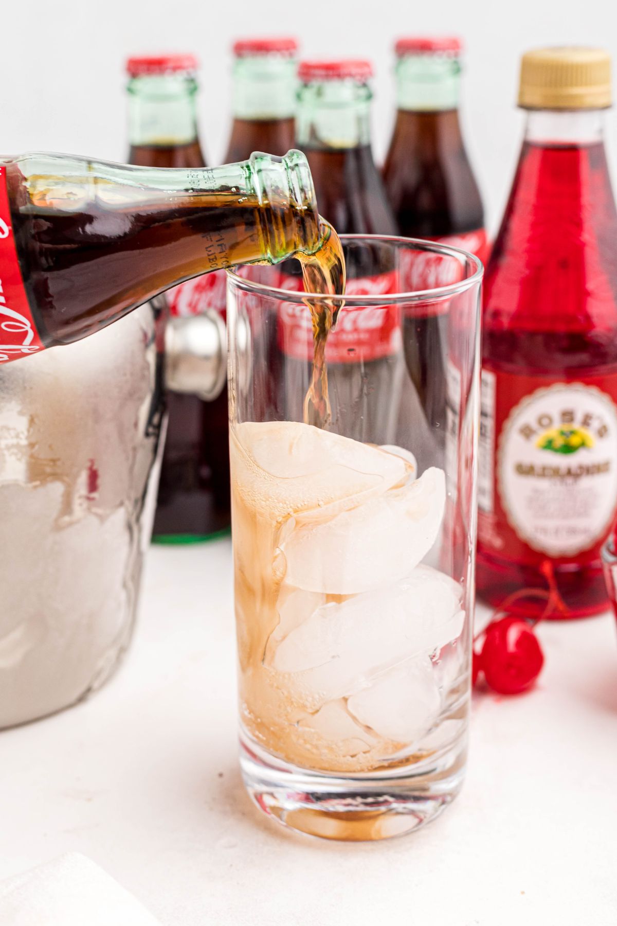 Cola being poured over ice in a large tall glass.
