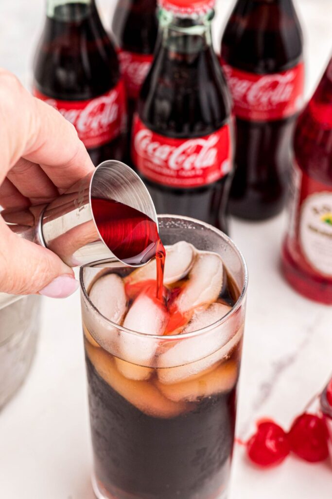 Grenadine syrup being poured over cola and ice in a high ball glass. 