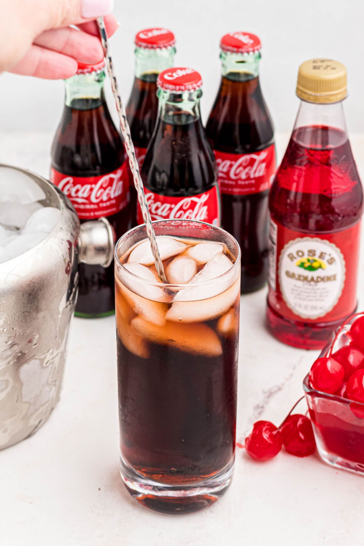 Cola and grenadine mixed in a glass filled with ice, and topped with cherries on a marble table.