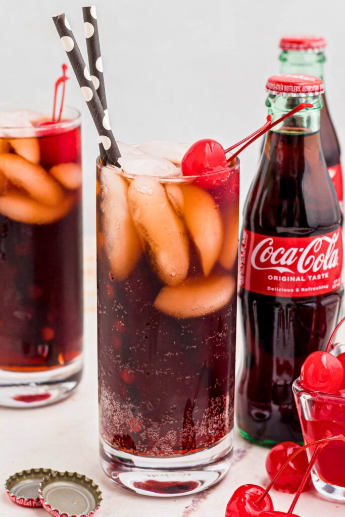 Clear glass of soda mixed with grenadine and ice, with cherries on top. 