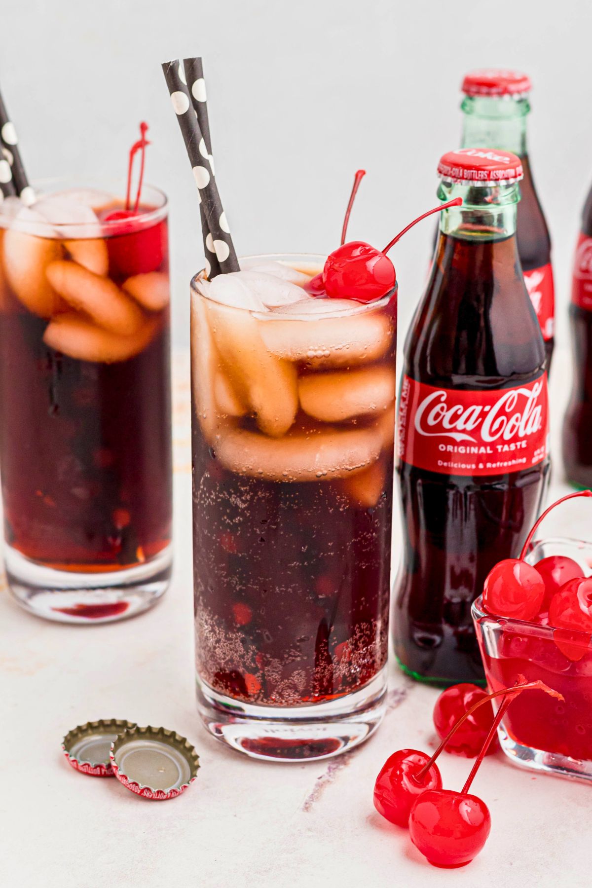 Cola and grenadine mixed in a glass filled with ice, and topped with cherries on a marble table.