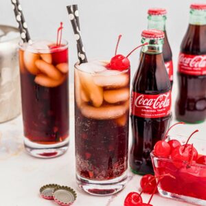 Cola and grenadine mixed in a glass filled with ice, and topped with cherries on a marble table.